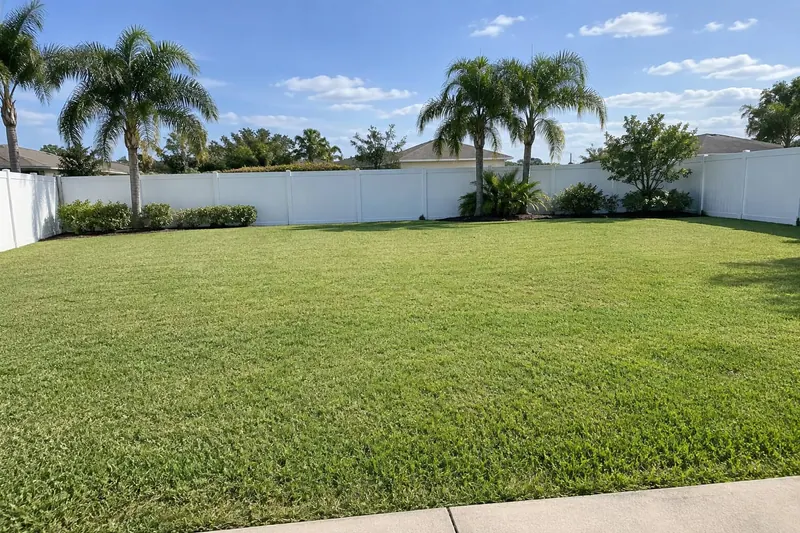 Un patio plano de Florida con césped, una cerca blanca y palmeras, sin piscina.